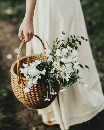 Woven basket of wildflowers held by a woman in a linen dress, symbolizing regenerative beauty and earthborn skincare