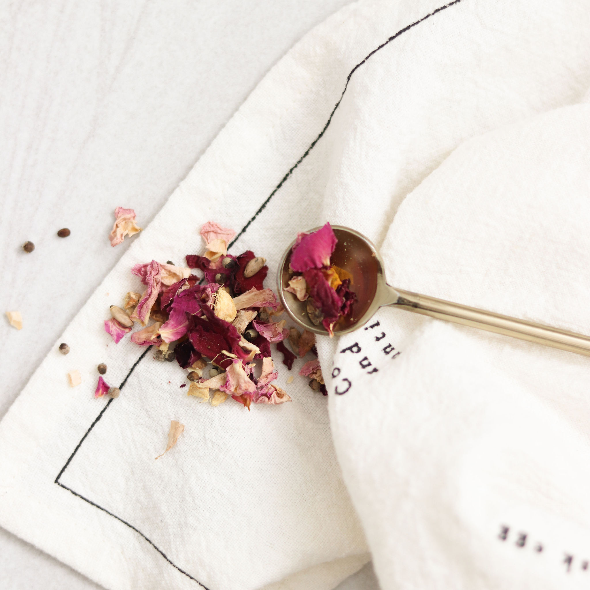 Wildcrafted rose petals and botanicals styled on linen with a gold spoon, reflecting earthborn, regenerative skincare ingredients.